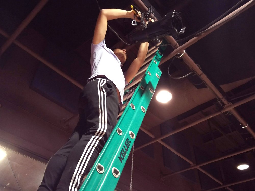 Gabe hangs and focuses a lighting instrument for in a word